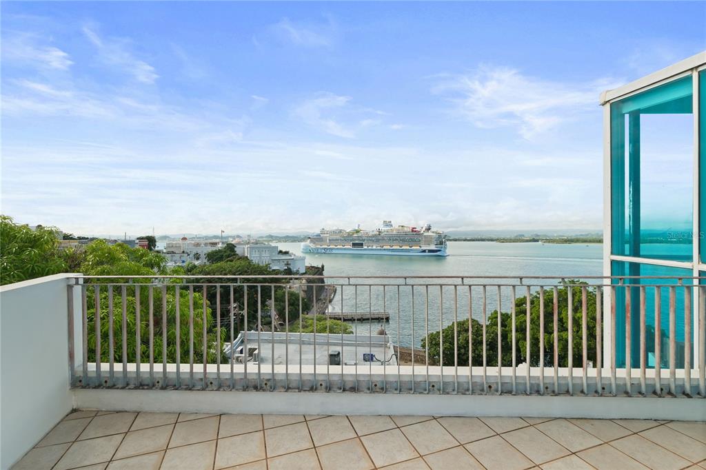 A balcony with a metal railing overlooks a harbor with a large cruise ship — 10 CALLE SOL, OLD SAN JUAN, PR