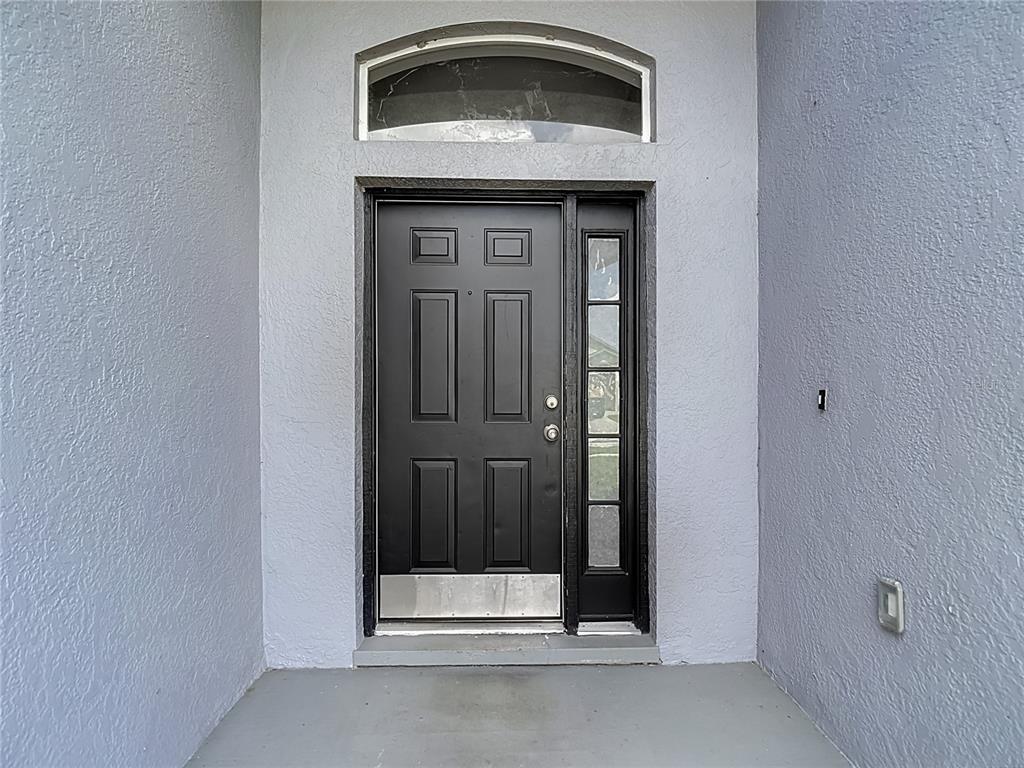A black front door with a side window and arched transom sits in a gray entryway — 1732 HULETT DRIVE, BRANDON, FL