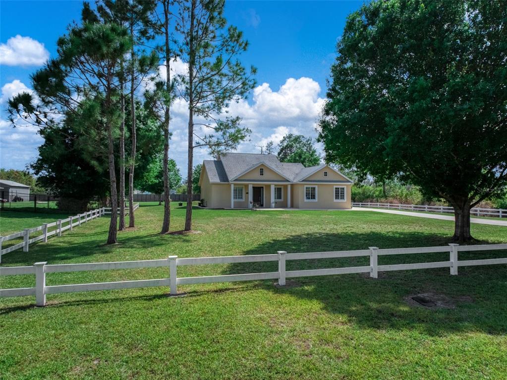 A single-story house with a beige exterior sits on a grassy lot with white fencing — 2009 FLOWER TERRACE, SEBRING, FL