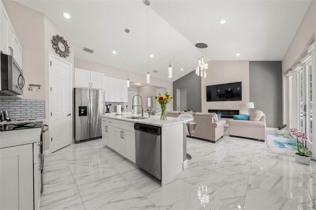 A bright open-concept kitchen and living area with white cabinetry, marble floors, and a fireplace — 2009 FLOWER TERRACE, SEBRING, FL