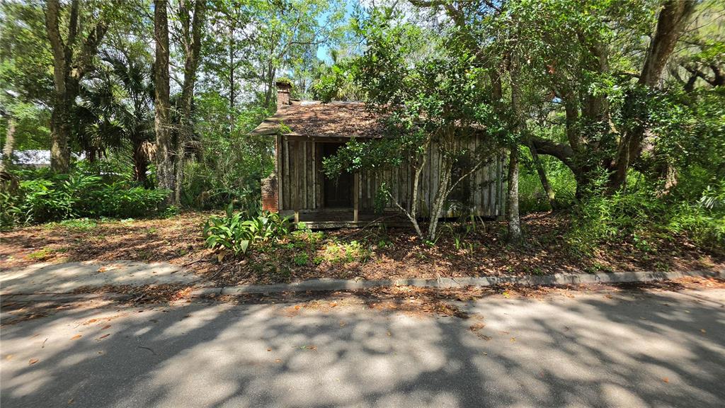 An old, weathered wooden cabin with a front porch sits among trees near a road — 304 NW 5TH STREET, MICANOPY, FL