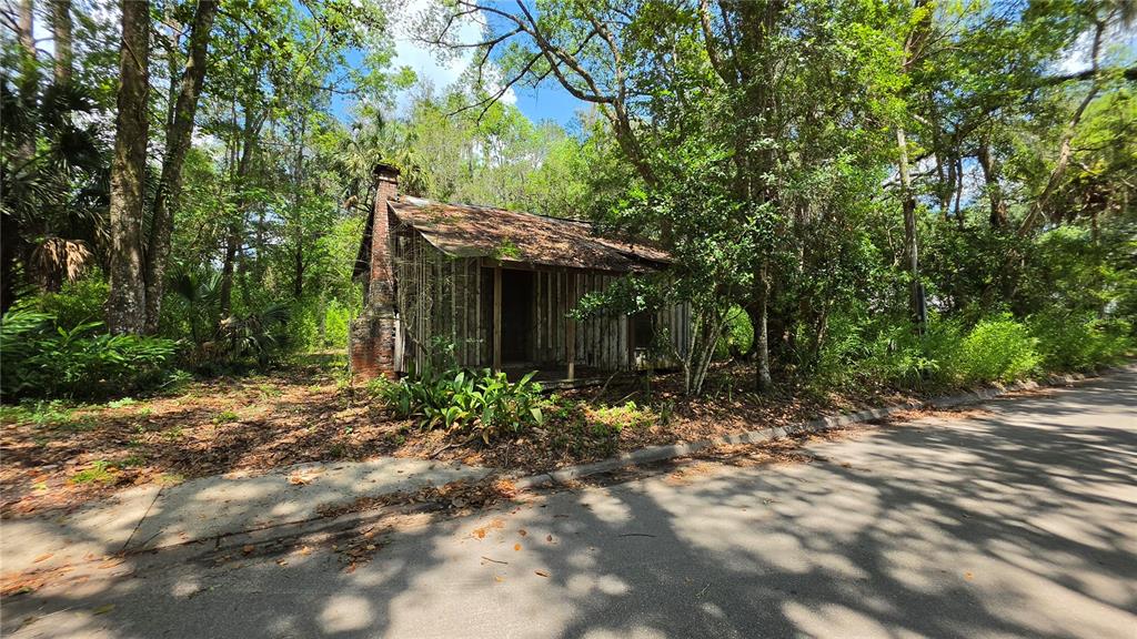An old, weathered wooden cabin with a brick chimney sits beside a paved road — 304 NW 5TH STREET, MICANOPY, FL