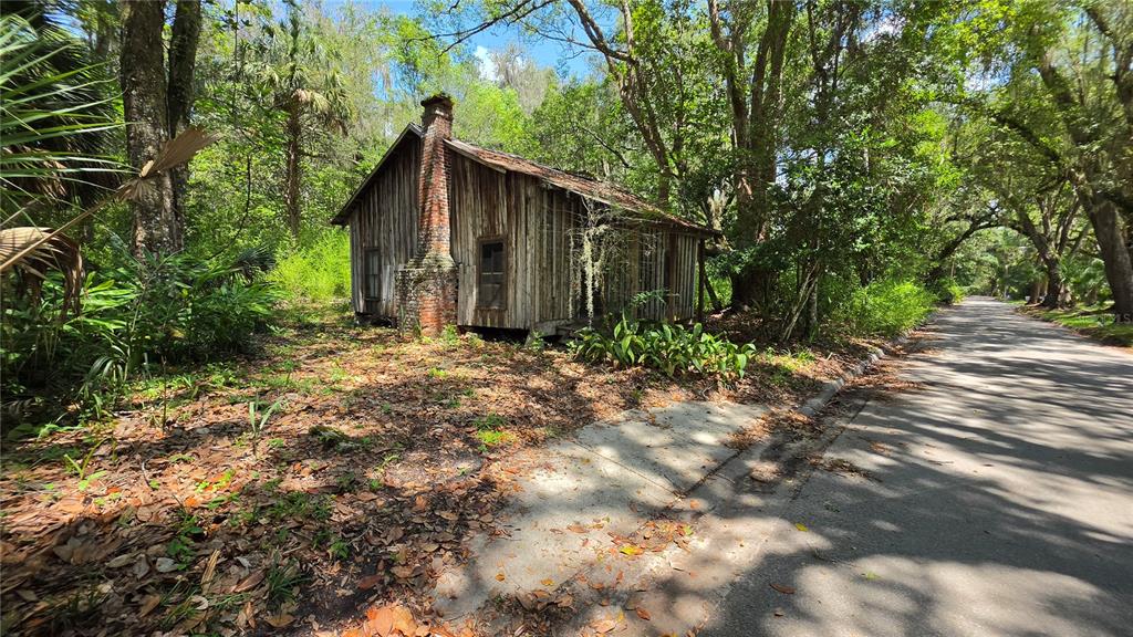 An old, weathered wooden cabin with a brick chimney sits beside a paved road — 304 NW 5TH STREET, MICANOPY, FL