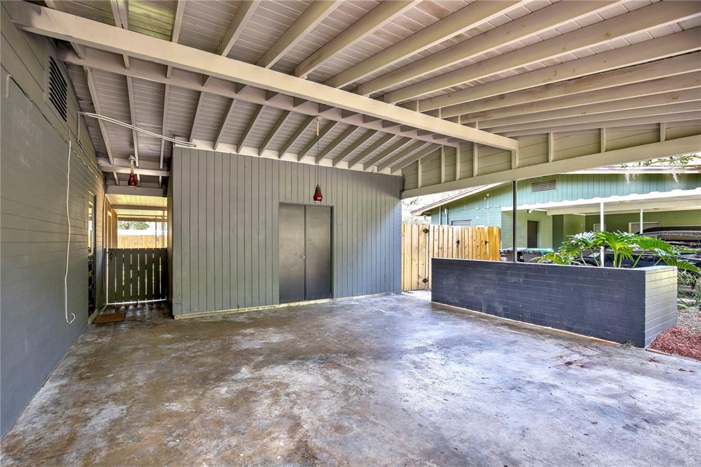 A covered concrete carport features a gray wood-paneled wall, a storage closet, and a planter — 2914 LANDO LANE, ORLANDO, FL