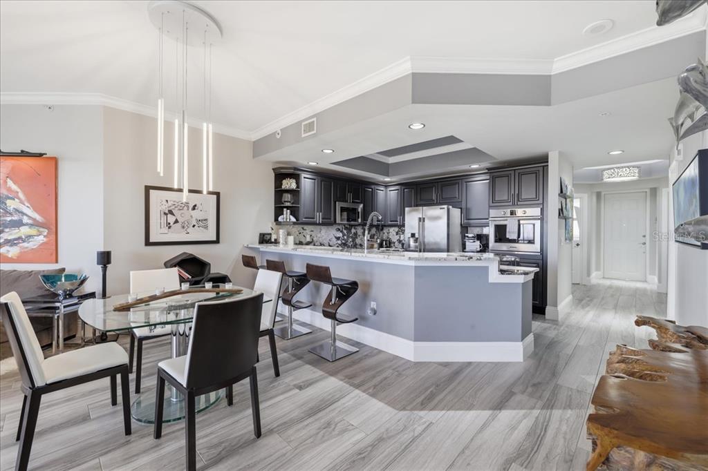 A modern kitchen with dark cabinetry and a breakfast bar overlooks a dining area — 14300 RIVA DEL LAGO DRIVE UNIT 1802, FORT MYERS, FL