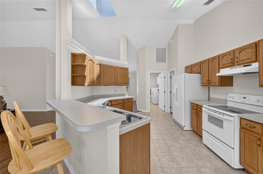 A kitchen with wood cabinets, white appliances, a breakfast bar, and tile flooring — 10976 SW 139TH COURT, DUNNELLON, FL