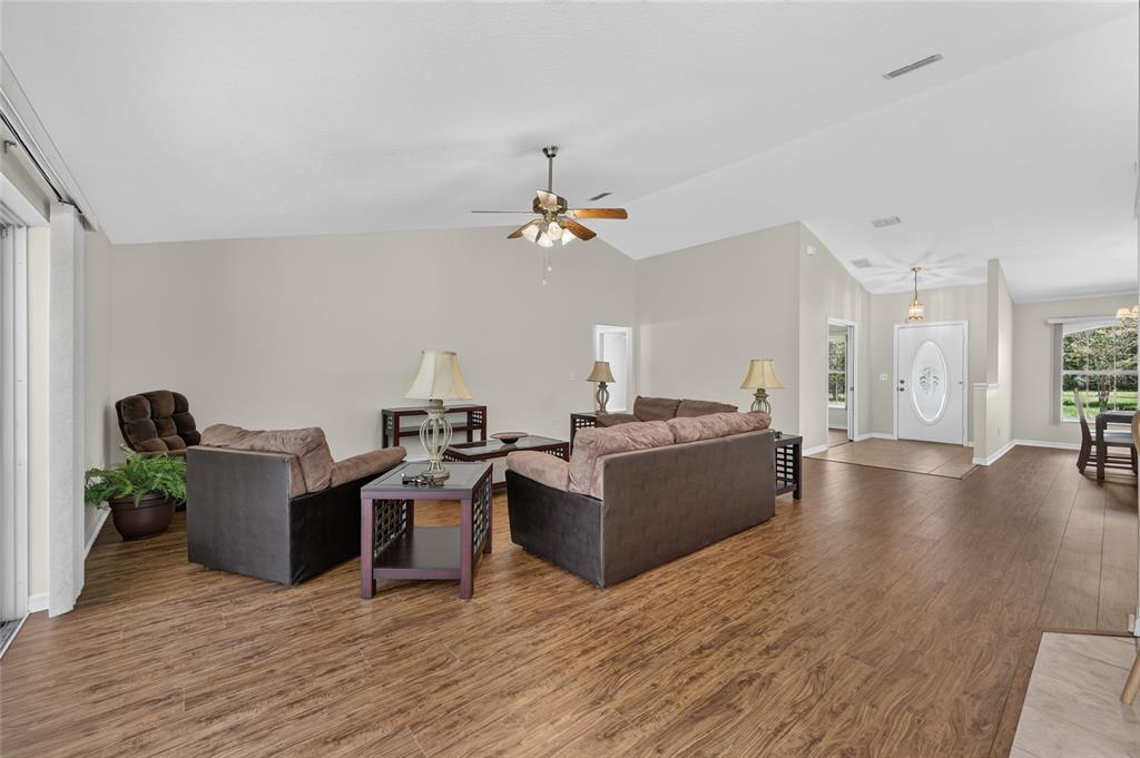 A living room features wood-look flooring, brown furniture, and a vaulted ceiling with a fan — 10976 SW 139TH COURT, DUNNELLON, FL