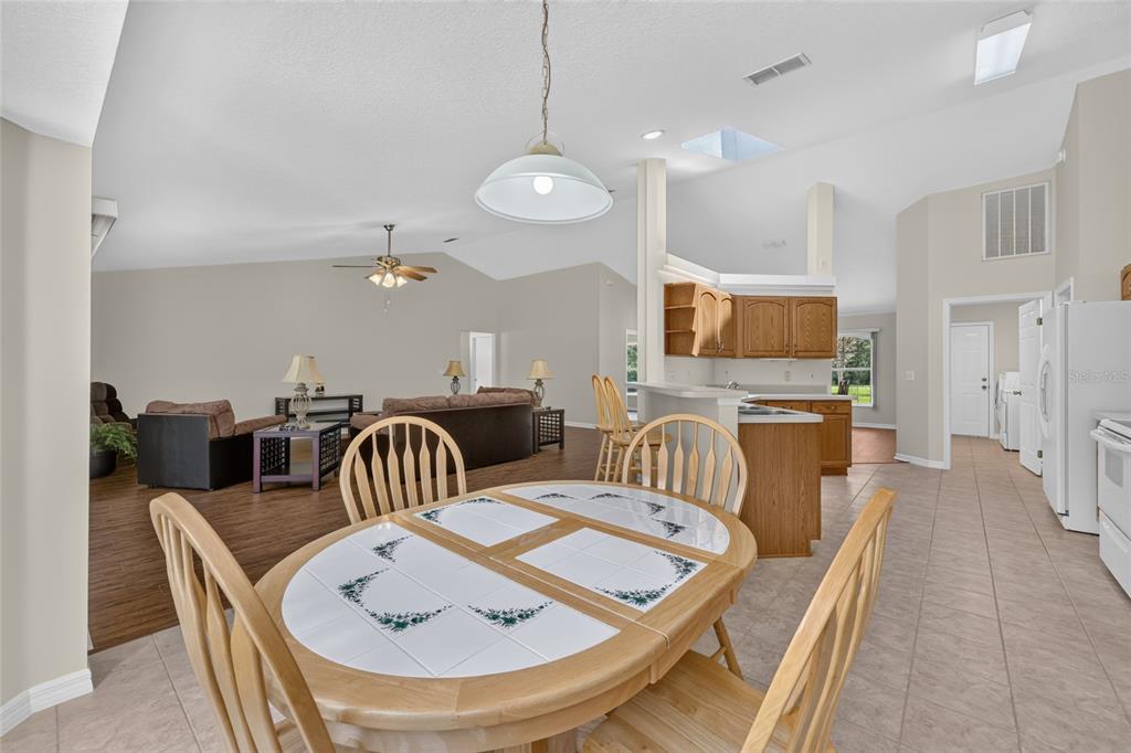 A dining area with a tiled table sits adjacent to an open kitchen and living room — 10976 SW 139TH COURT, DUNNELLON, FL