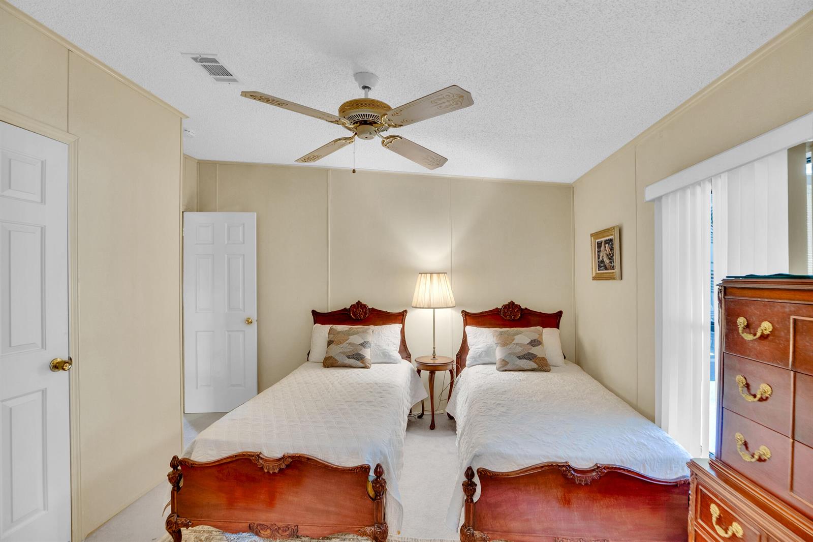 A bedroom features two twin beds with wooden headboards, a central nightstand, and a ceiling fan — FL