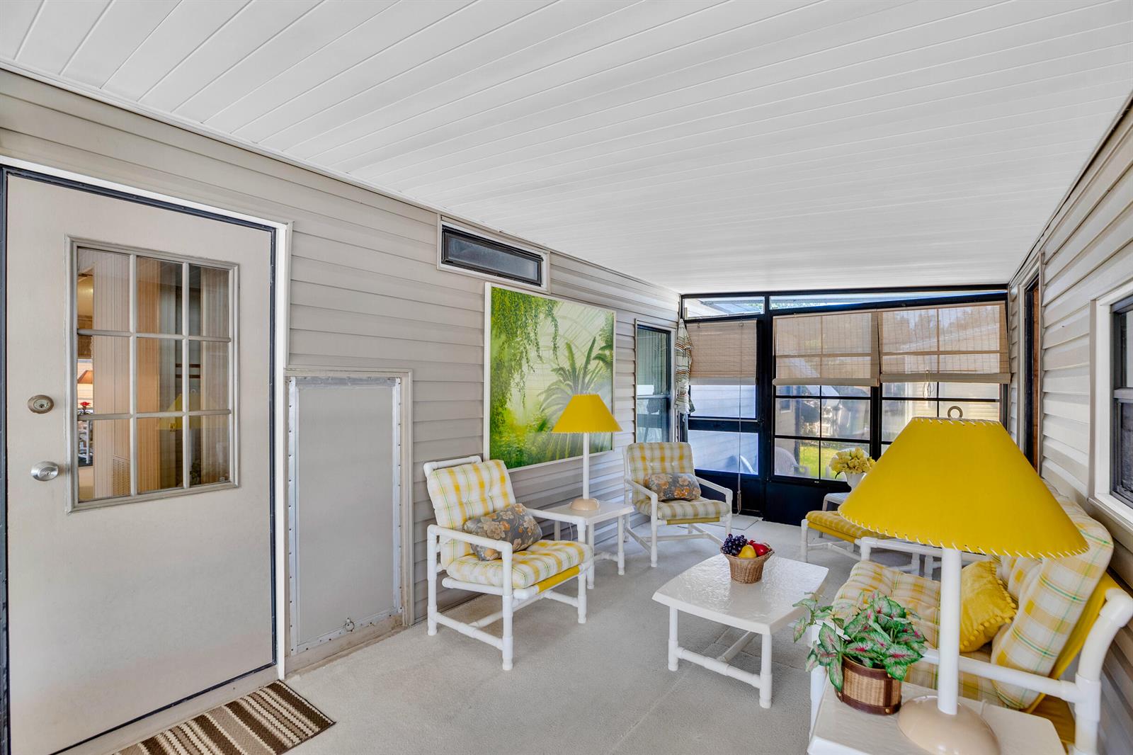 A sunroom features light-colored siding, a white ceiling, and a seating area with yellow furniture — FL
