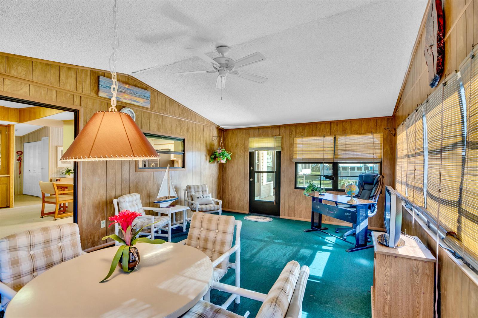 A sunroom with wood-paneled walls, green carpeting, a ceiling fan, and a dining area — FL