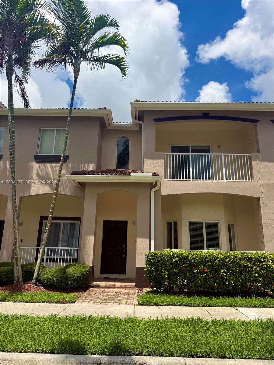 A two-story townhouse exterior with a brick walkway, palm trees, and a second-floor balcony — 1947 SE 23rd Rd, Homestead FL 33035, HOMESTEAD, FL