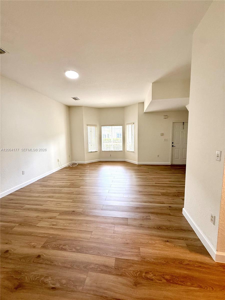 An empty living room features light wood-look flooring, white walls, and a bay window — 1947 SE 23rd Rd, Homestead FL 33035, HOMESTEAD, FL