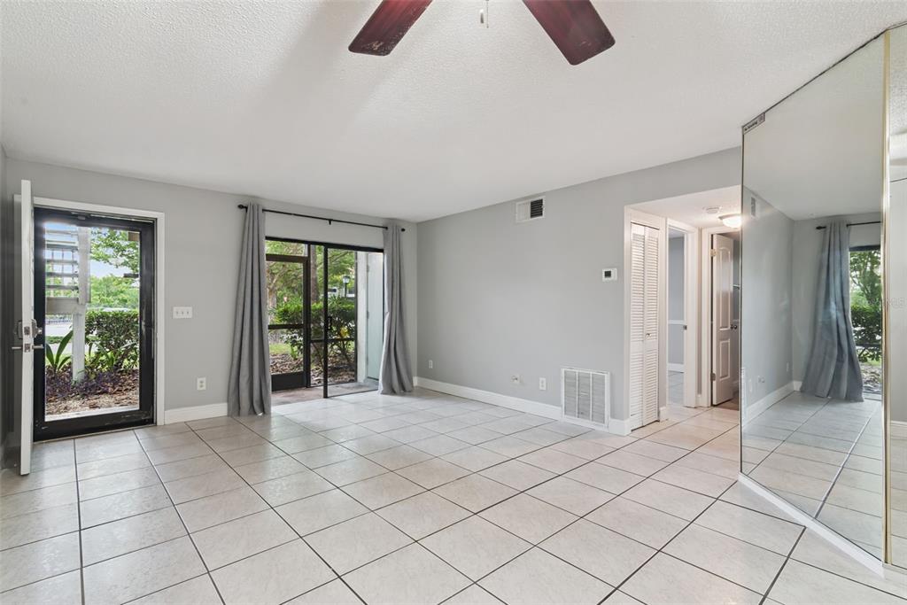 An empty living room with light tile flooring, a sliding glass door, and mirrored walls — 7302 SWALLOW RUN UNIT 7302, WINTER PARK, FL