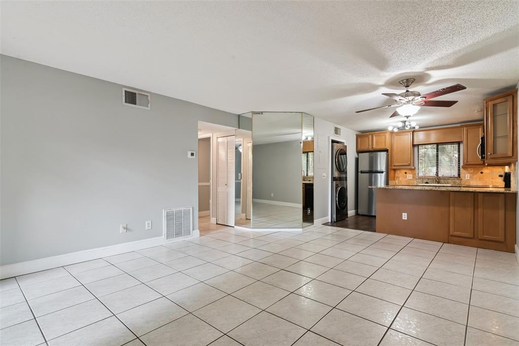 A tiled living area features a mirrored wall, a kitchen with wooden cabinets, and appliances — 7302 SWALLOW RUN UNIT 7302, WINTER PARK, FL