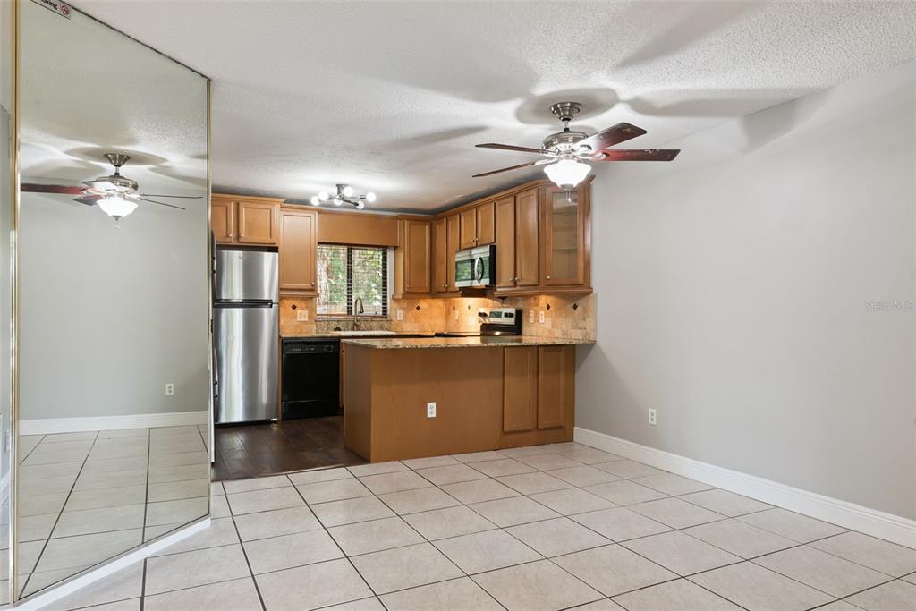 A kitchen with wood cabinets, granite countertops, and tile flooring opens to a dining area — 7302 SWALLOW RUN UNIT 7302, WINTER PARK, FL