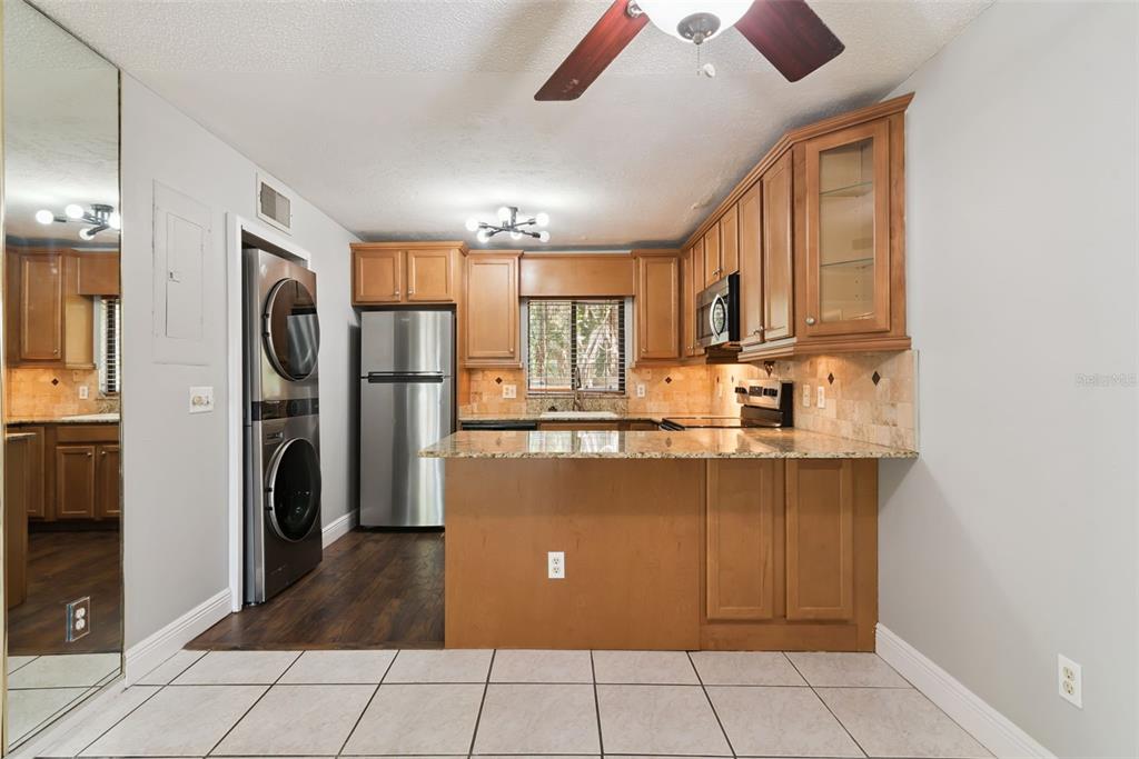 A kitchen with wood cabinets, granite countertops, stainless steel appliances, and a stacked washer-dryer unit — 7302 SWALLOW RUN UNIT 7302, WINTER PARK, FL