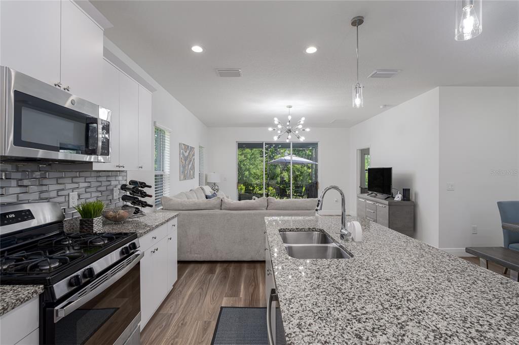 A kitchen with granite countertops and white cabinets overlooks a living area with a sofa — 4848 DEEP CREEK TERRACE, PARRISH, FL