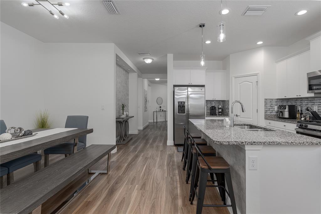 A modern kitchen and dining area with white cabinets, granite countertops, and wood-look flooring — 4848 DEEP CREEK TERRACE, PARRISH, FL