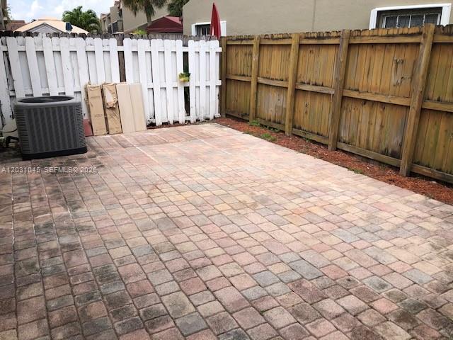 A paved patio area features a central air conditioning unit and a wooden privacy fence — 6230 SW 129 PL # 1210, Miami FL 33183, MIAMI, FL