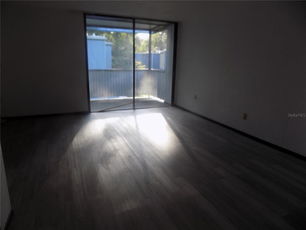 An empty room with wood-look flooring and a sliding glass door leading to a balcony — 613 SW 75 STREET UNIT 101, GAINESVILLE, FL