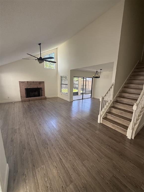 A living room with wood-look flooring, a brick fireplace, vaulted ceilings, and a wooden staircase — 1859 SPRINGWOOD CIRCLE N, CLEARWATER, FL