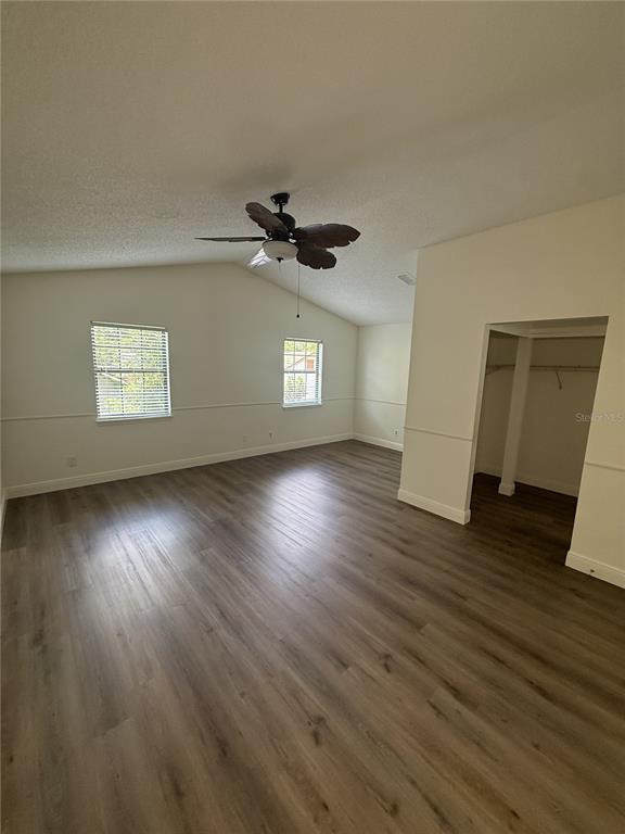 An empty bedroom features wood-look flooring, a vaulted ceiling with a fan, and a walk-in closet — 1859 SPRINGWOOD CIRCLE N, CLEARWATER, FL