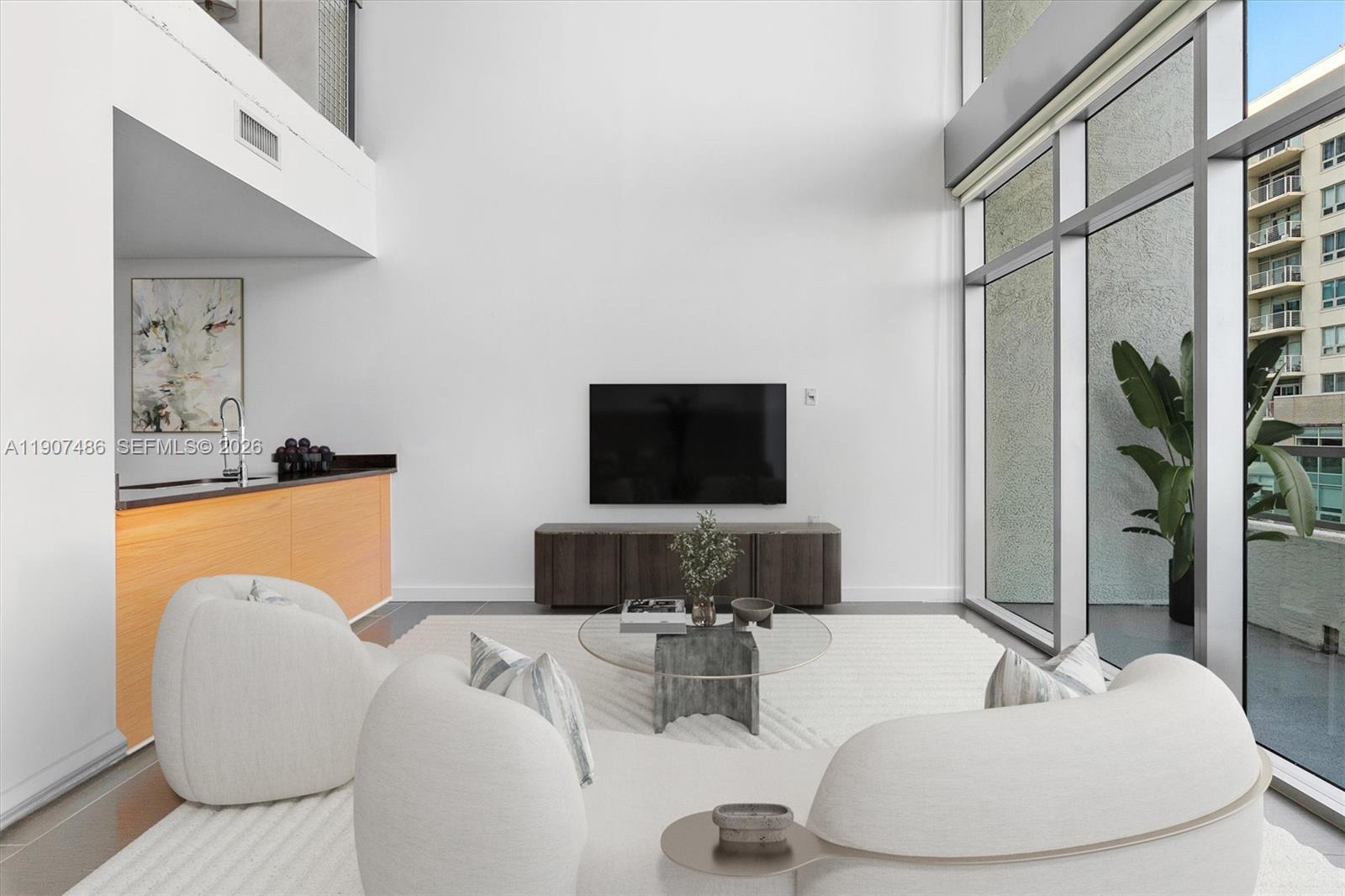 A modern living room features a curved white sofa, floor-to-ceiling windows, and a metal staircase — 3301 NE 1st Ave # M0502, Miami FL 33137, MIAMI, FL