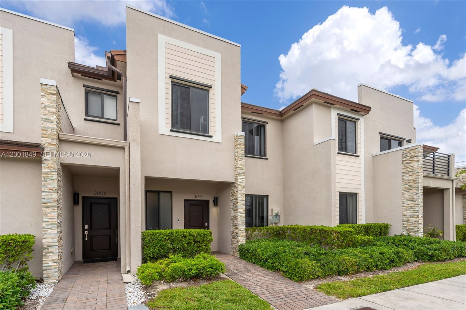 The exterior of two adjacent townhomes features tan stucco walls, stone accents, and paved walkways — 21444 NE 2nd Path, Miami FL 33179, MIAMI, FL