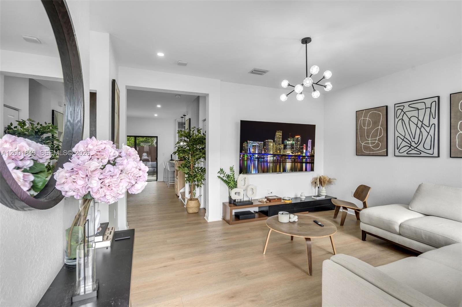 A modern living room features a wall-mounted television, light wood flooring, and a chandelier — 21444 NE 2nd Path, Miami FL 33179, MIAMI, FL