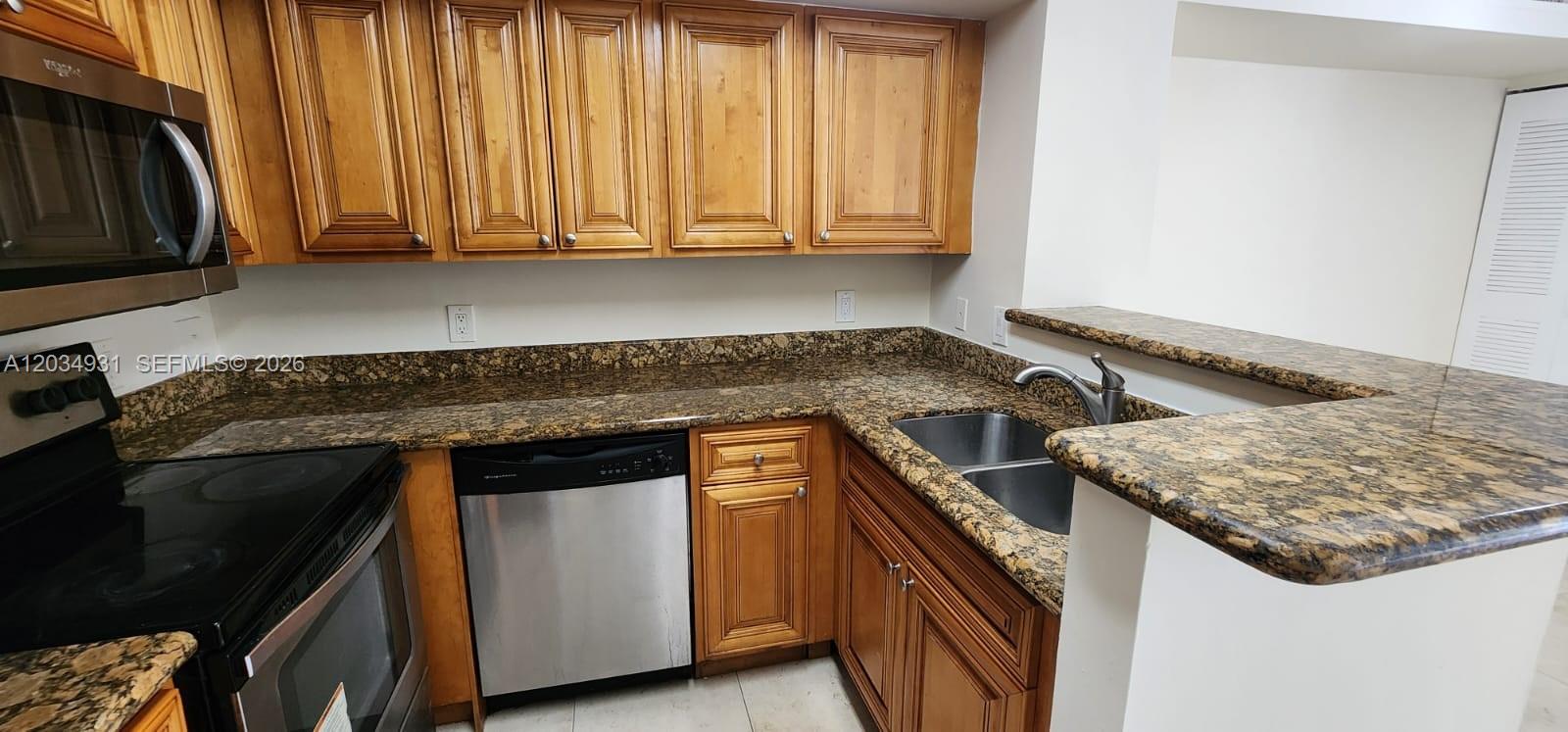 A kitchen features wood cabinets, granite countertops, a stainless steel dishwasher, and a double sink — 12154 Saint Andrews Pl # 110, Miramar FL 33025, MIRAMAR, FL