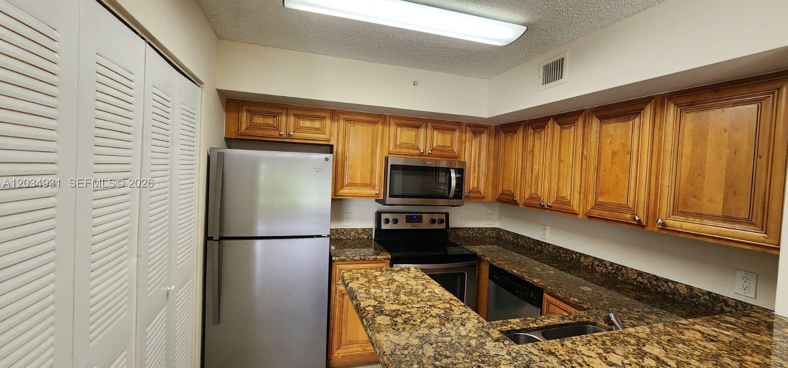 A kitchen features wood cabinets, granite countertops, and stainless steel appliances — 12154 Saint Andrews Pl # 110, Miramar FL 33025, MIRAMAR, FL