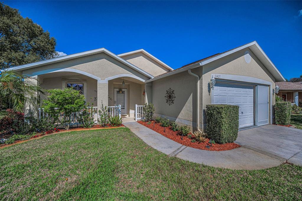 A single-story house with a beige stucco exterior, a front porch, and an attached garage — 11427 TURTLE DOVE PLACE, NEW PORT RICHEY, FL