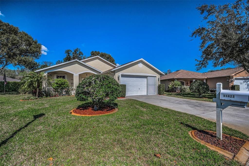 A single-story suburban house with a tan stucco exterior, a two-car garage, and a lawn — 11427 TURTLE DOVE PLACE, NEW PORT RICHEY, FL