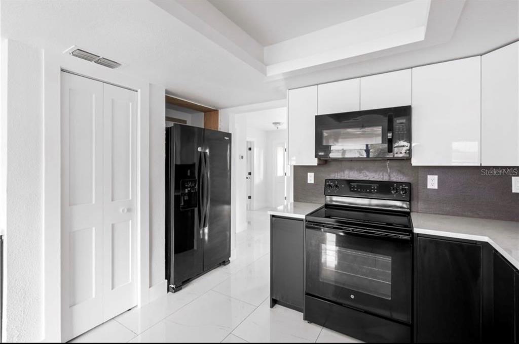 A kitchen features white upper cabinets, black lower cabinets, black appliances, and white tile flooring — 3381 MINNOW CREEK DRIVE, HERNANDO BEACH, FL