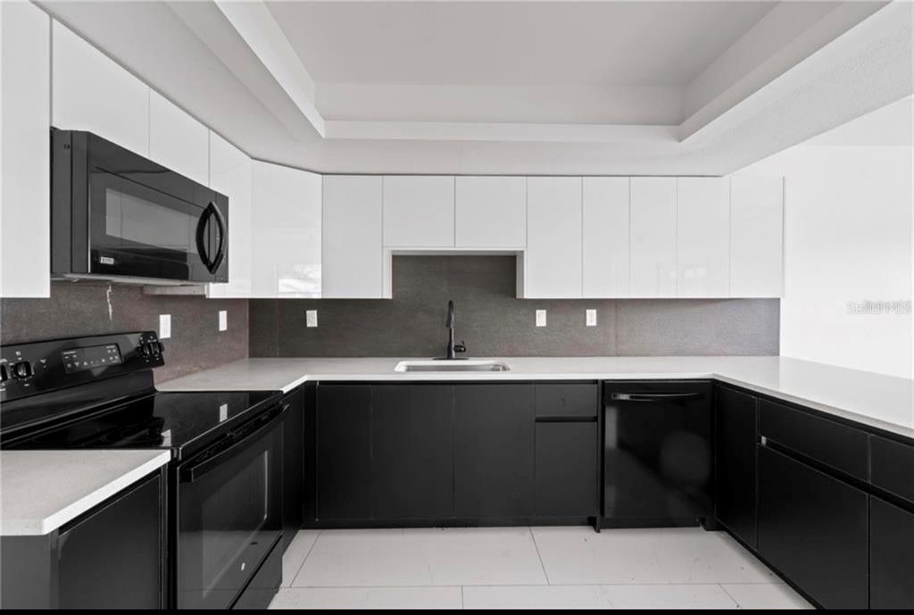 A modern kitchen features black lower cabinets, white upper cabinets, and a dark tile backsplash — 3381 MINNOW CREEK DRIVE, HERNANDO BEACH, FL