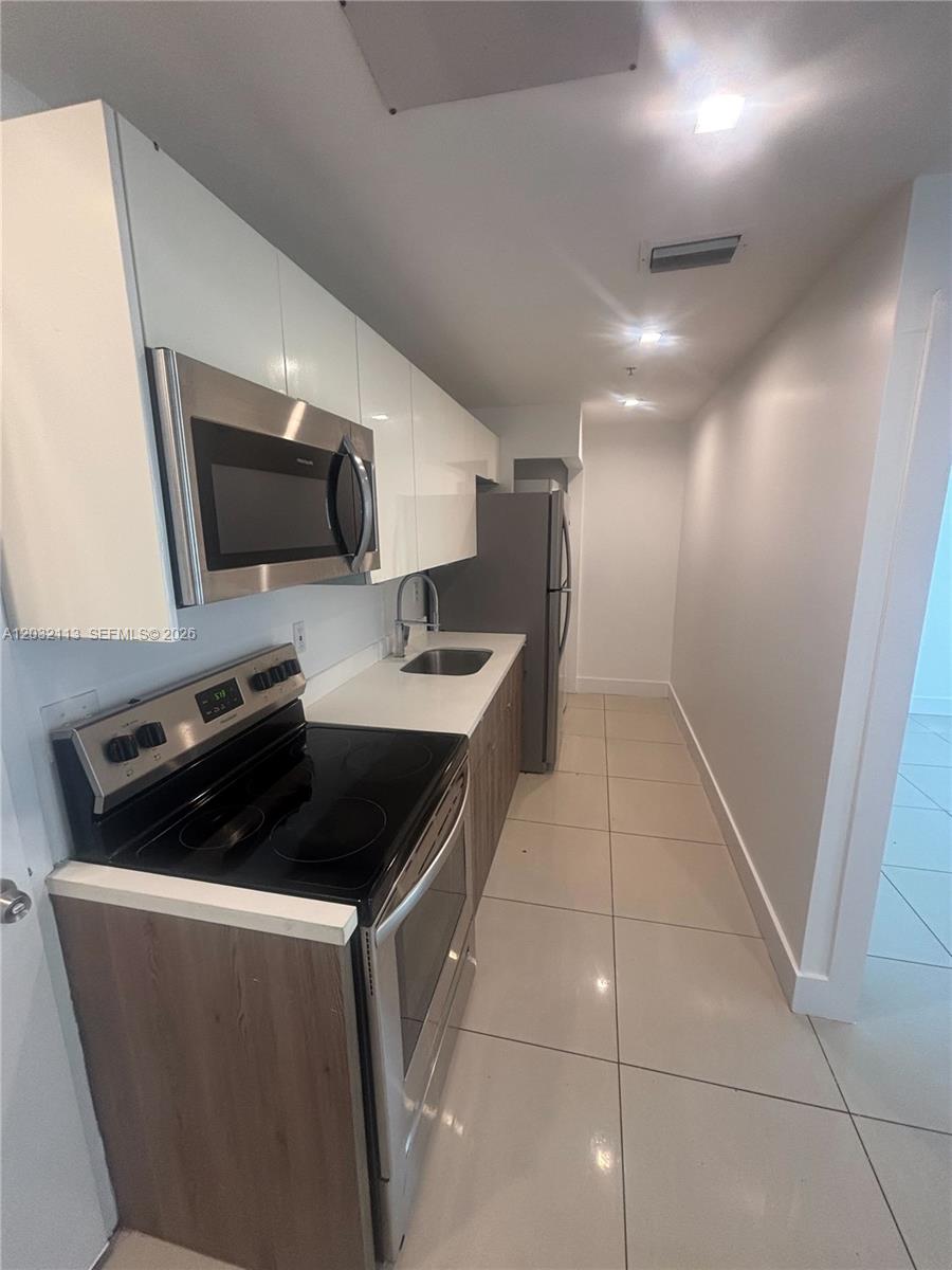 A galley-style kitchen features white upper cabinets, wood-tone lower cabinets, and stainless steel appliances — 821 SW 18th Ave # 203, Miami FL 33135, MIAMI, FL