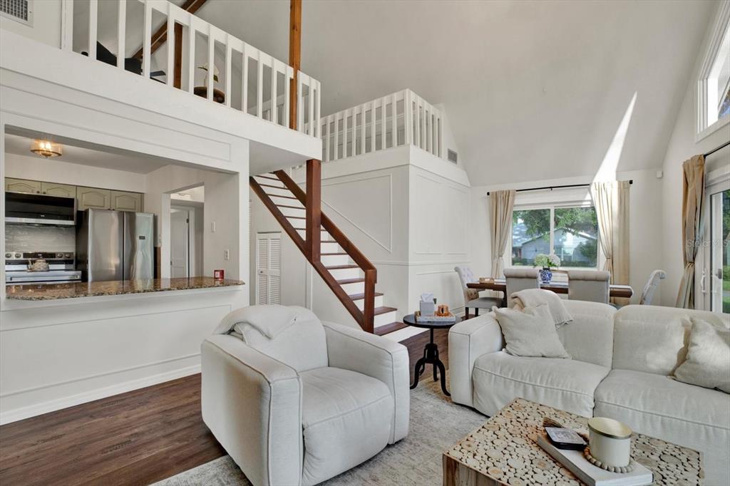 A living room with a loft, wooden staircase, white furniture, and an open kitchen area — 7295 HUBERT STREET, SEMINOLE, FL