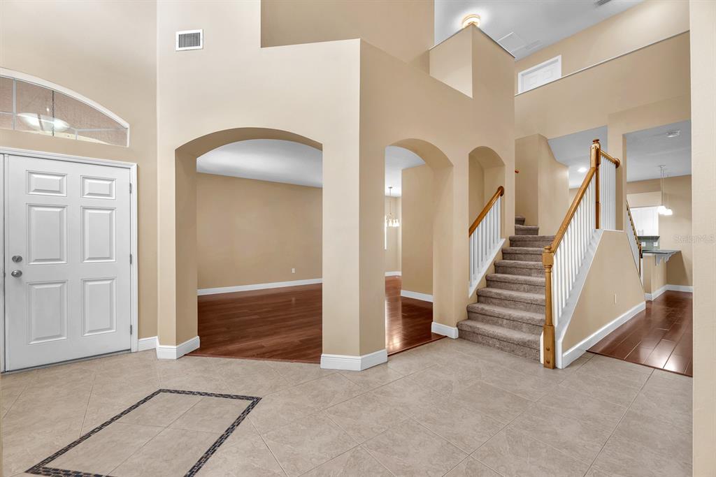 A foyer with tile flooring, arched doorways, a carpeted staircase, and hardwood flooring beyond — 10904 SUMMERTON DRIVE, RIVERVIEW, FL