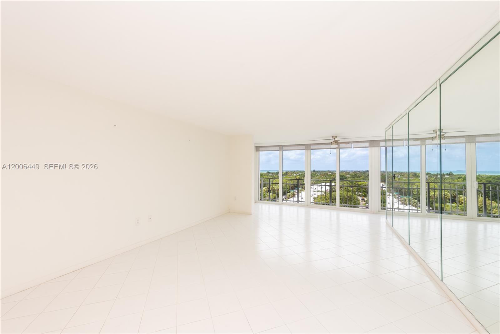 An empty room features white tile floors, a mirrored wall, and floor-to-ceiling windows — 600 Grapetree Dr, Key Biscayne FL 33149, KEY BISCAYNE, FL
