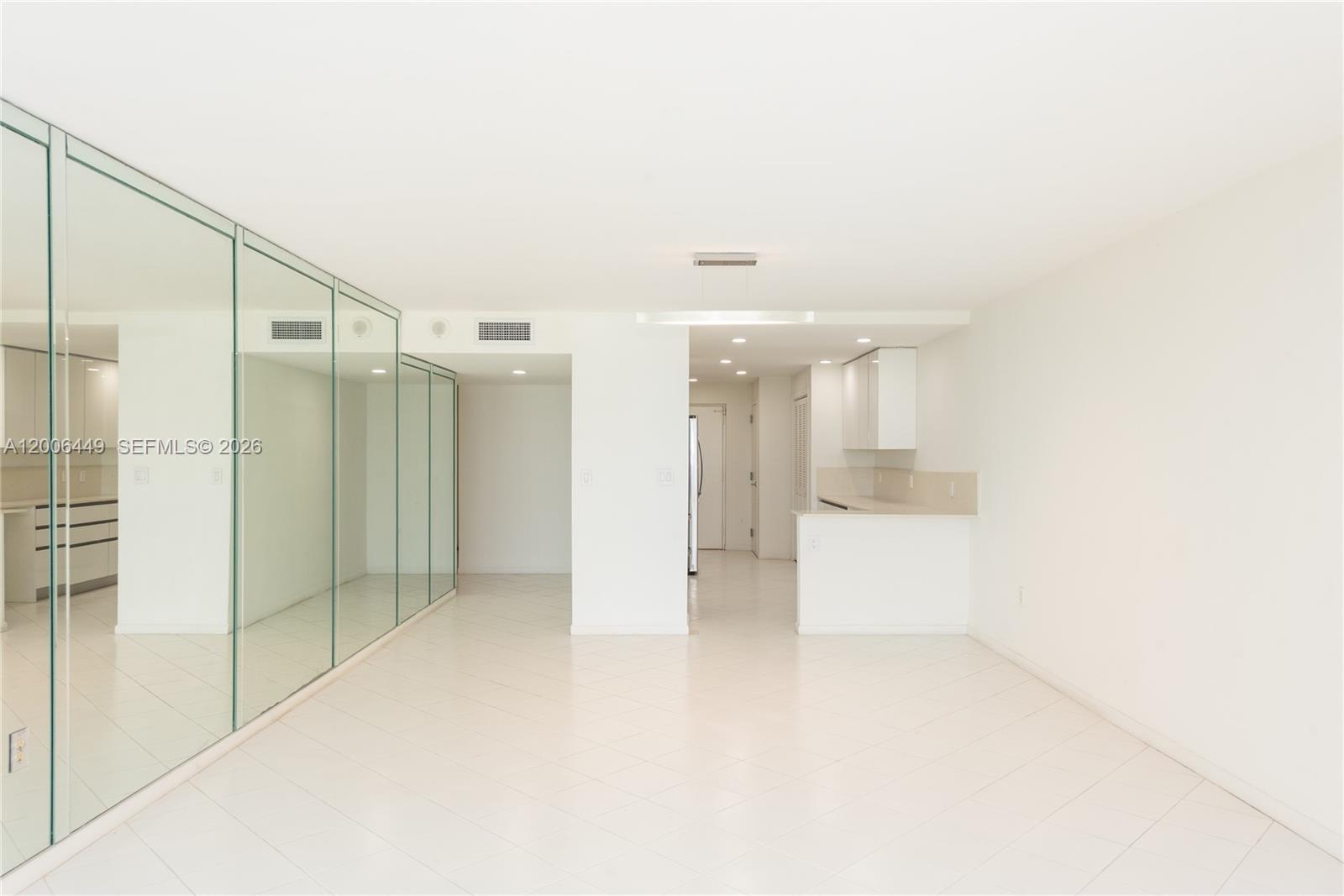 A bright, empty room features white tile floors, mirrored walls, and an open kitchen area — 600 Grapetree Dr, Key Biscayne FL 33149, KEY BISCAYNE, FL
