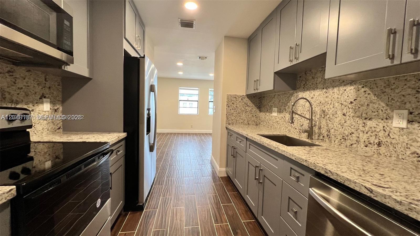 A galley kitchen features gray cabinets, granite countertops, and stainless steel appliances — 2130 Funston St # 2130, Hollywood FL 33020, HOLLYWOOD, FL
