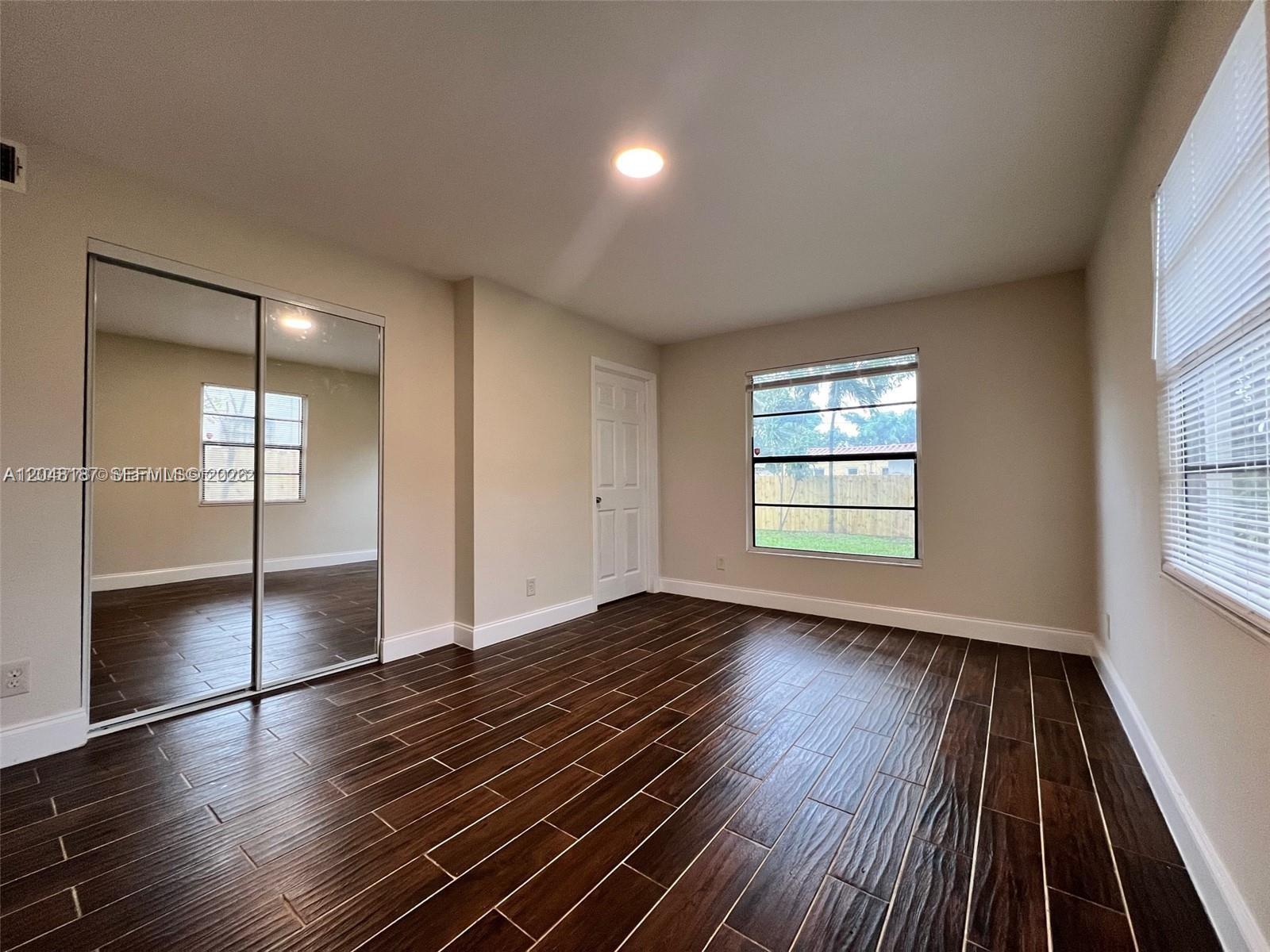 A bedroom features dark wood-look tile flooring, mirrored closet doors, and two windows — 2130 Funston St # 2130, Hollywood FL 33020, HOLLYWOOD, FL
