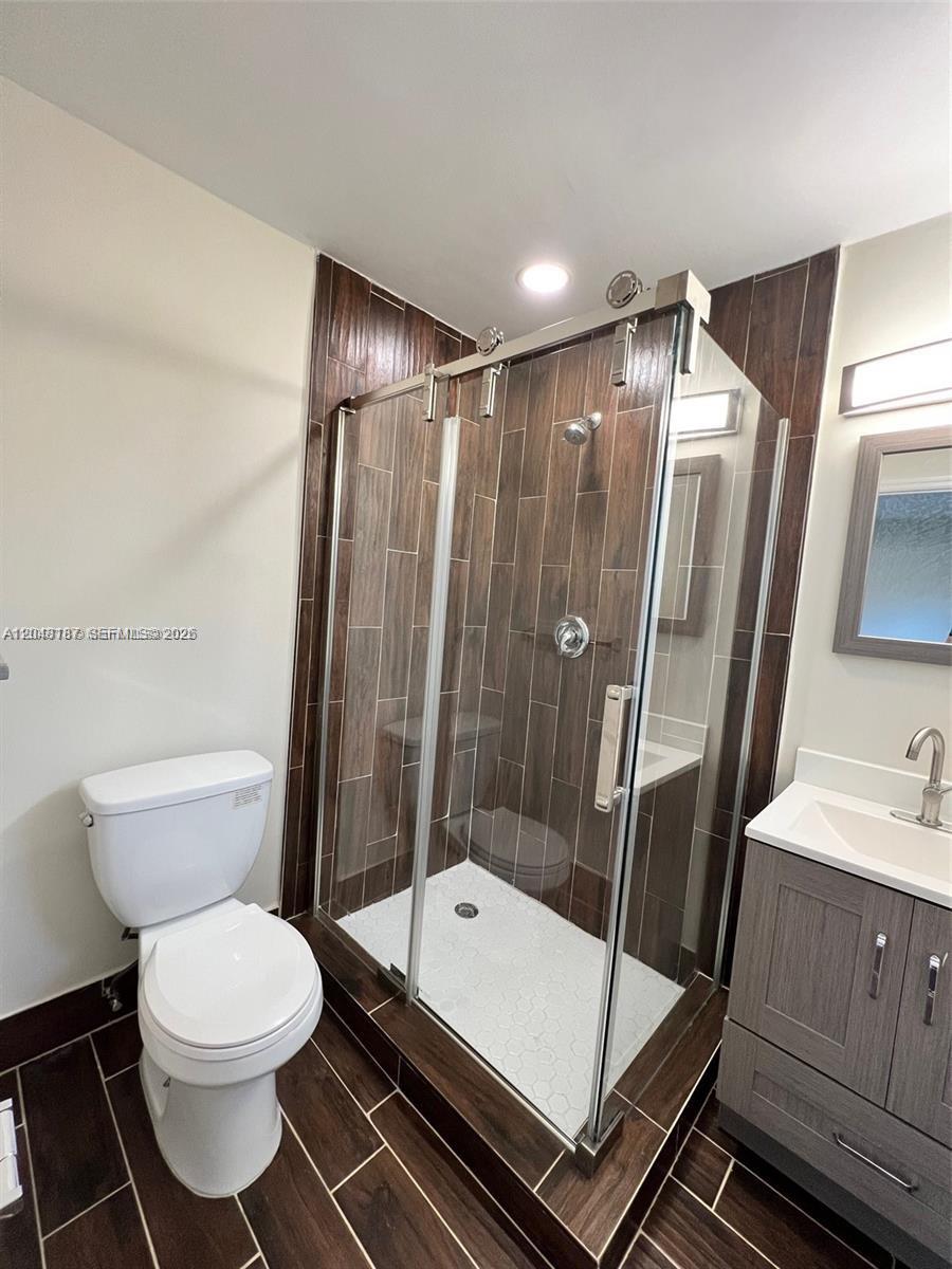 A bathroom features a glass-enclosed shower with wood-look tile, a white toilet, and a vanity — 2130 Funston St # 2130, Hollywood FL 33020, HOLLYWOOD, FL