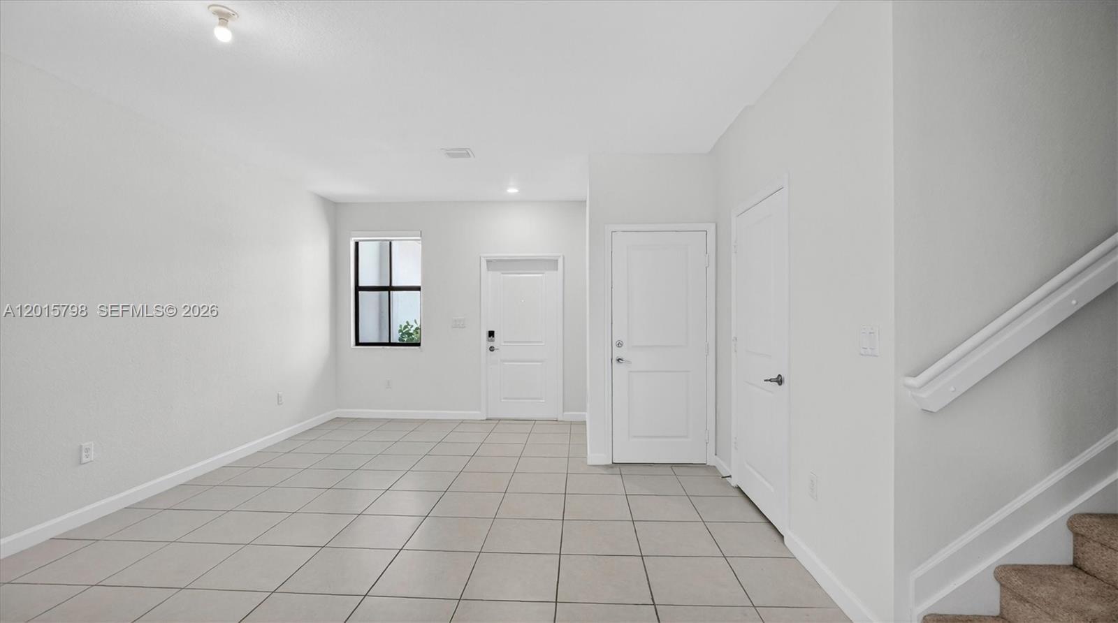 An empty room features white walls, light-colored tile flooring, two interior doors, and a staircase — 23029 SW 128th Pl, Miami FL 33170, MIAMI, FL