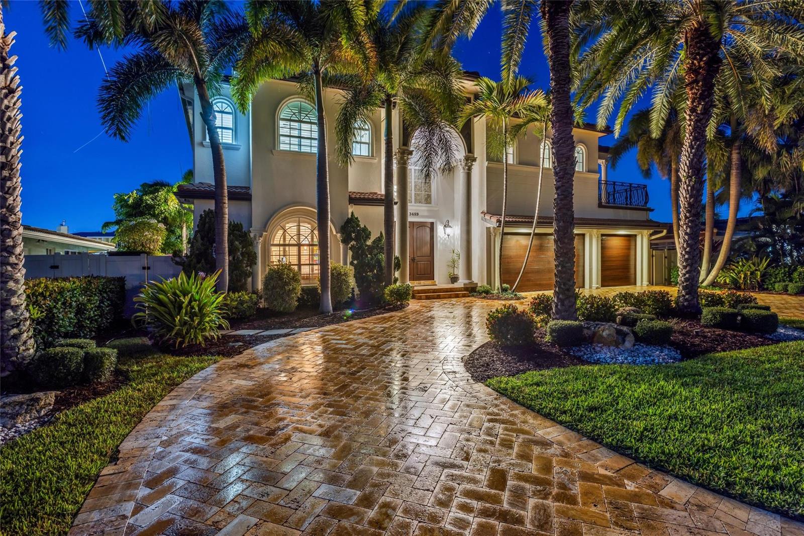 A two-story Mediterranean-style house with a paved driveway, palm trees, and illuminated garage doors — 3489 NE 30th Avenue, Lighthouse Point FL 33064, LIGHTHOUSE POINT, FL