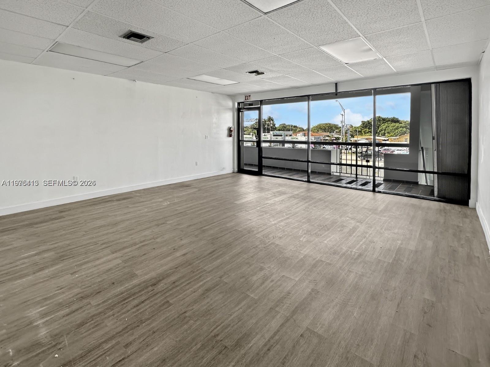 An empty commercial office space features wood-look flooring, a drop ceiling, and large glass windows — 497 NW 27th Ave # 497, Miami FL 33125, MIAMI, FL