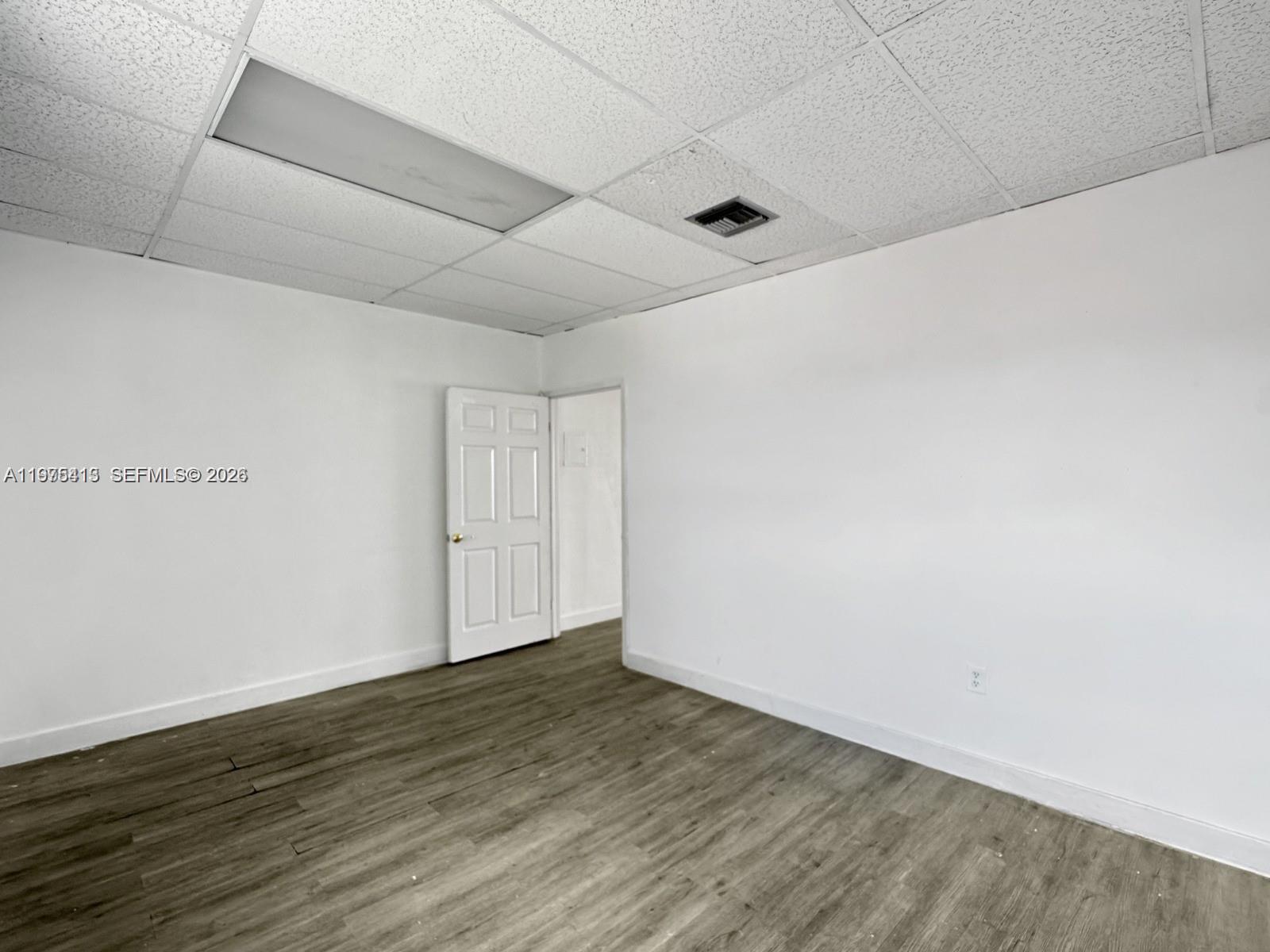 An empty room features white walls, a drop ceiling with a light fixture, and wood-look flooring — 497 NW 27th Ave # 497, Miami FL 33125, MIAMI, FL