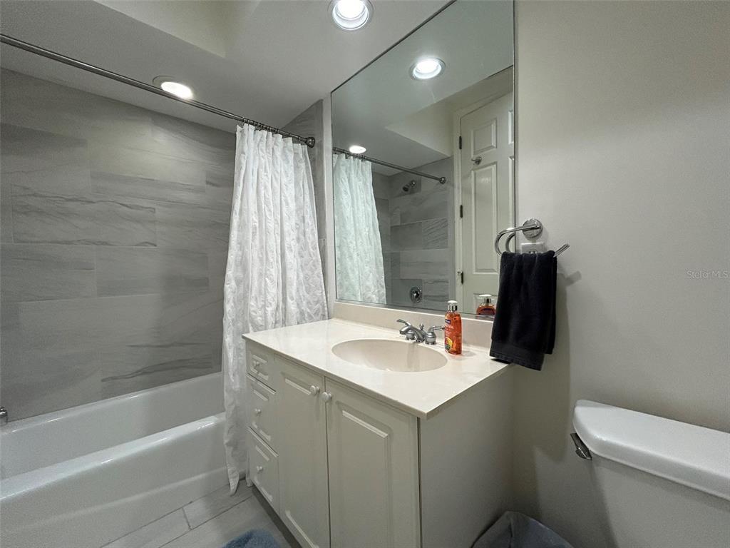 A bathroom features a white vanity, a mirror, and a shower-tub combination with tiled walls — 3705 54TH DRIVE W UNIT 201, BRADENTON, FL