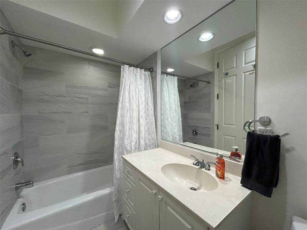 A bathroom features a white vanity, a large mirror, and a tiled shower-tub combination — 3705 54TH DRIVE W UNIT 201, BRADENTON, FL
